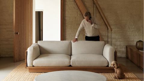 John Pawson standing behind an ivory Pawson Drift Sofa in a living room with a dog.
